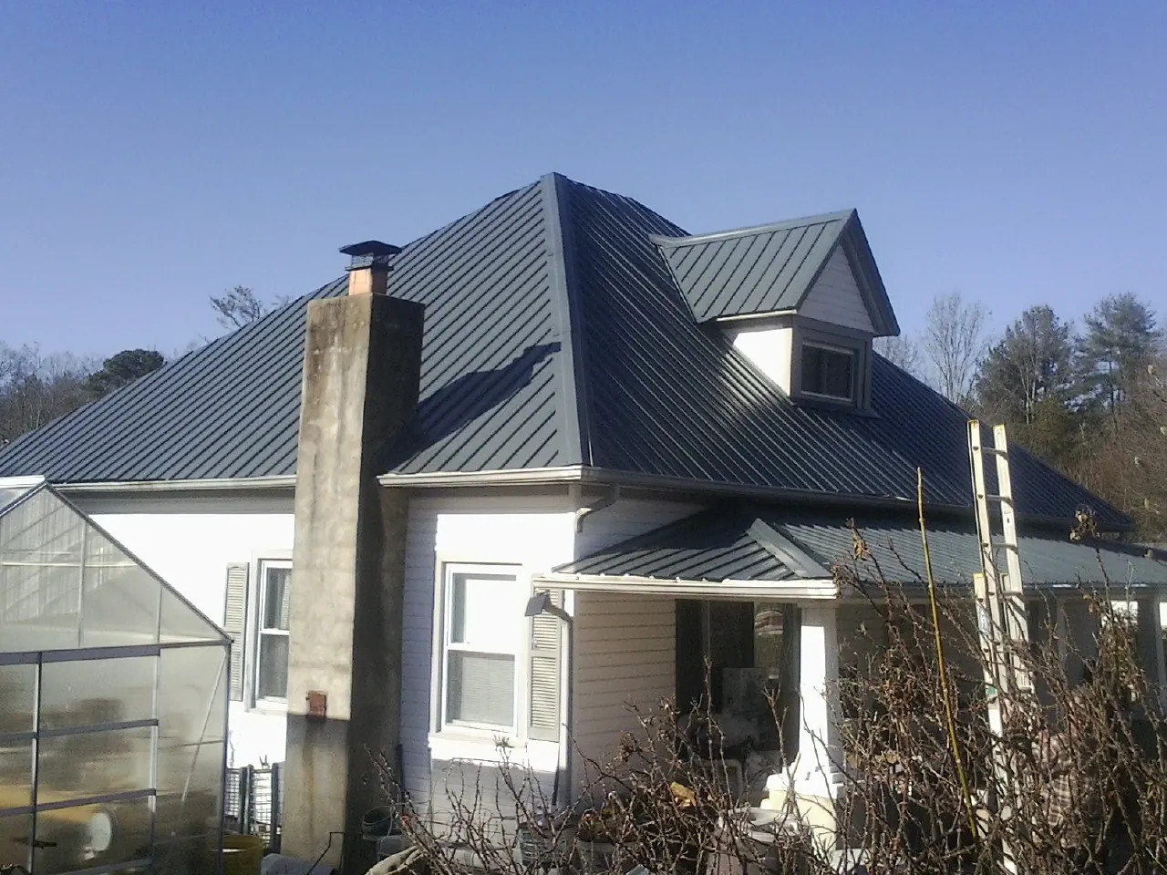 Dark blue standing seam metal roof on a white farmhouse with dormer — Slate & Tile Roof Repair by Roofing Brothers in Nottingham