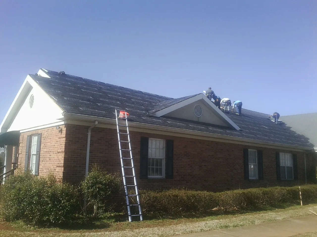 Crew tearing shingles off a brick ranch roof with a ladder set — Metal Roof Repair work by our crew in Nottingham